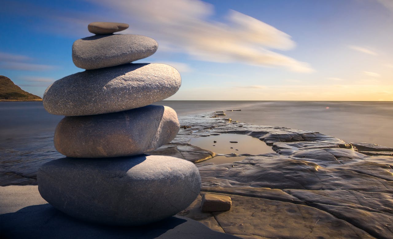 A serene wellness spa setup with pieces of stone put on top each other on the rock, in front the sea, that the clear blue sky connect to the sea.